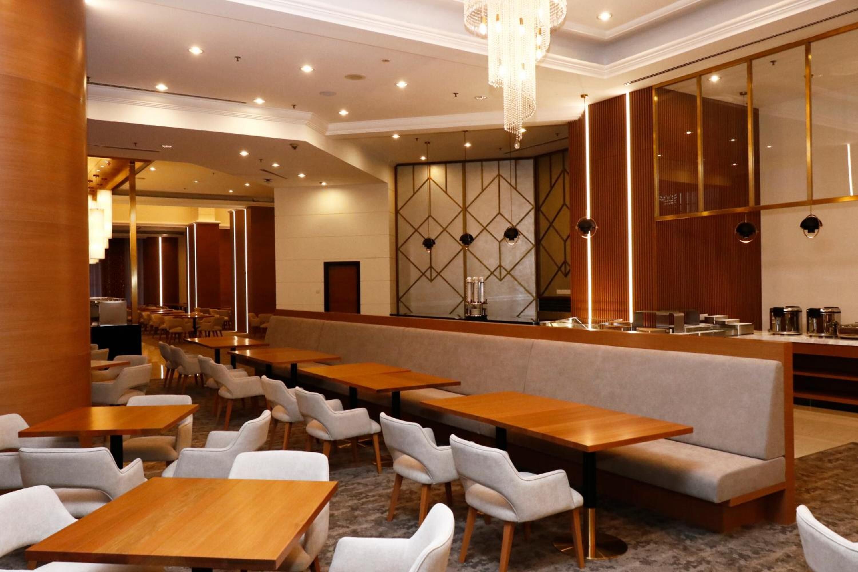 Een moderne hotellobby met lange tafels en stoelen, een bar en een decoratieve muur met geometrische patronen.