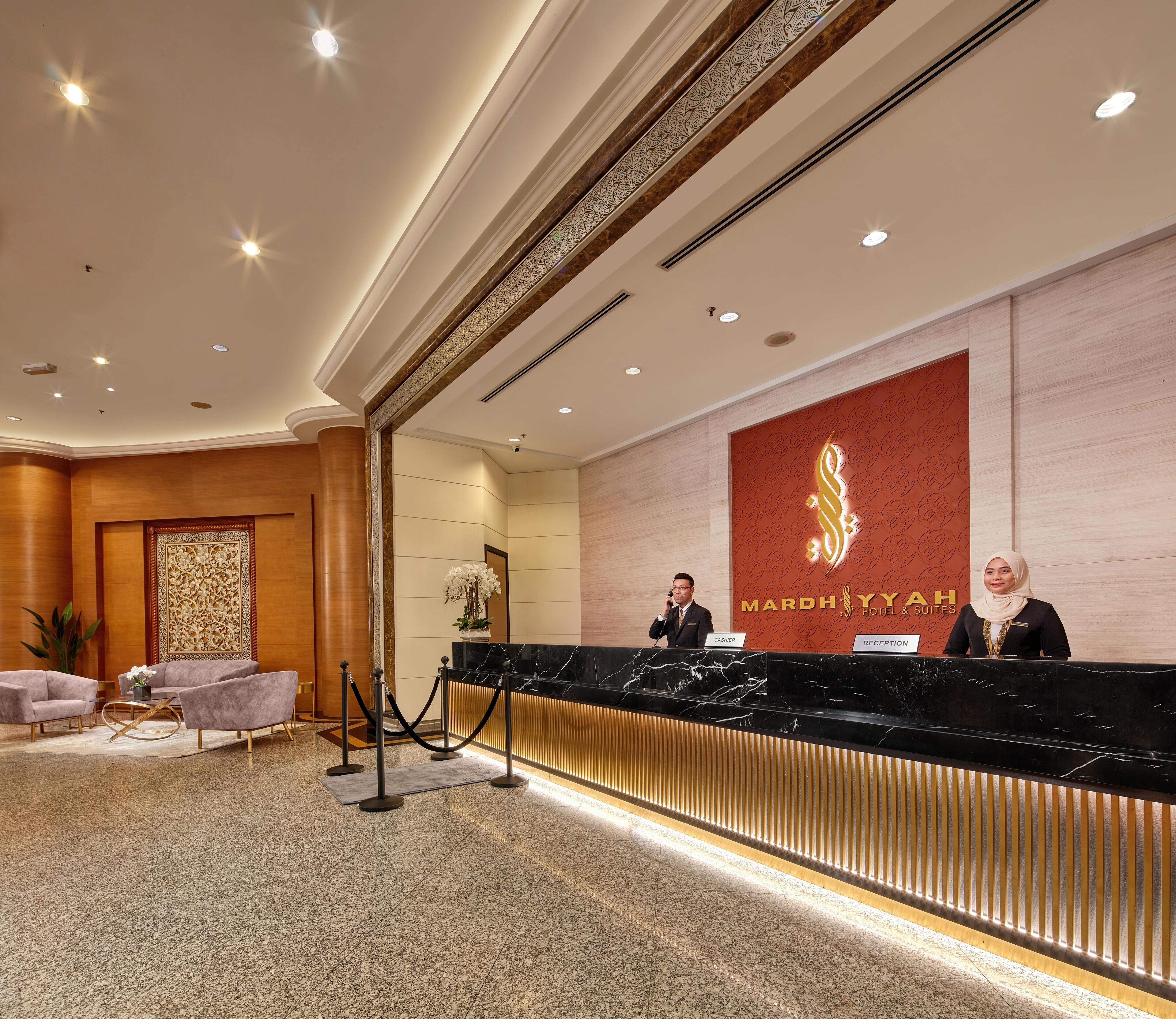 Zona de recepción de un hotel con mostrador de mármol, dos empleados y un mostrador de atención al cliente.