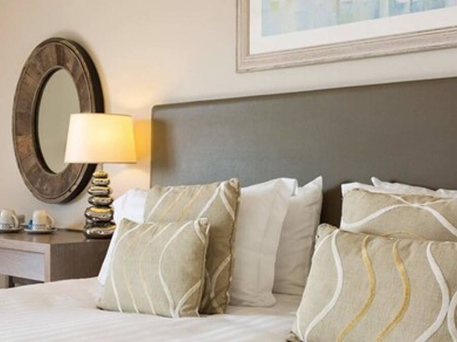A hotel room with a neatly made bed, a bedside lamp, a mirror, and a framed picture on the wall.