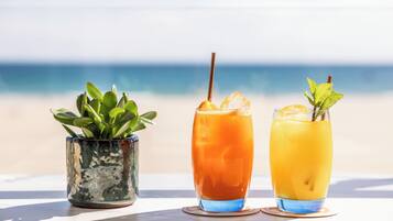 Two drinks on a table with a plant and a beach view in the background.