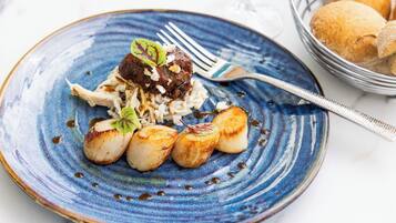 A plate with seared scallops, a piece of meat, and a garnish on a blue ceramic plate.