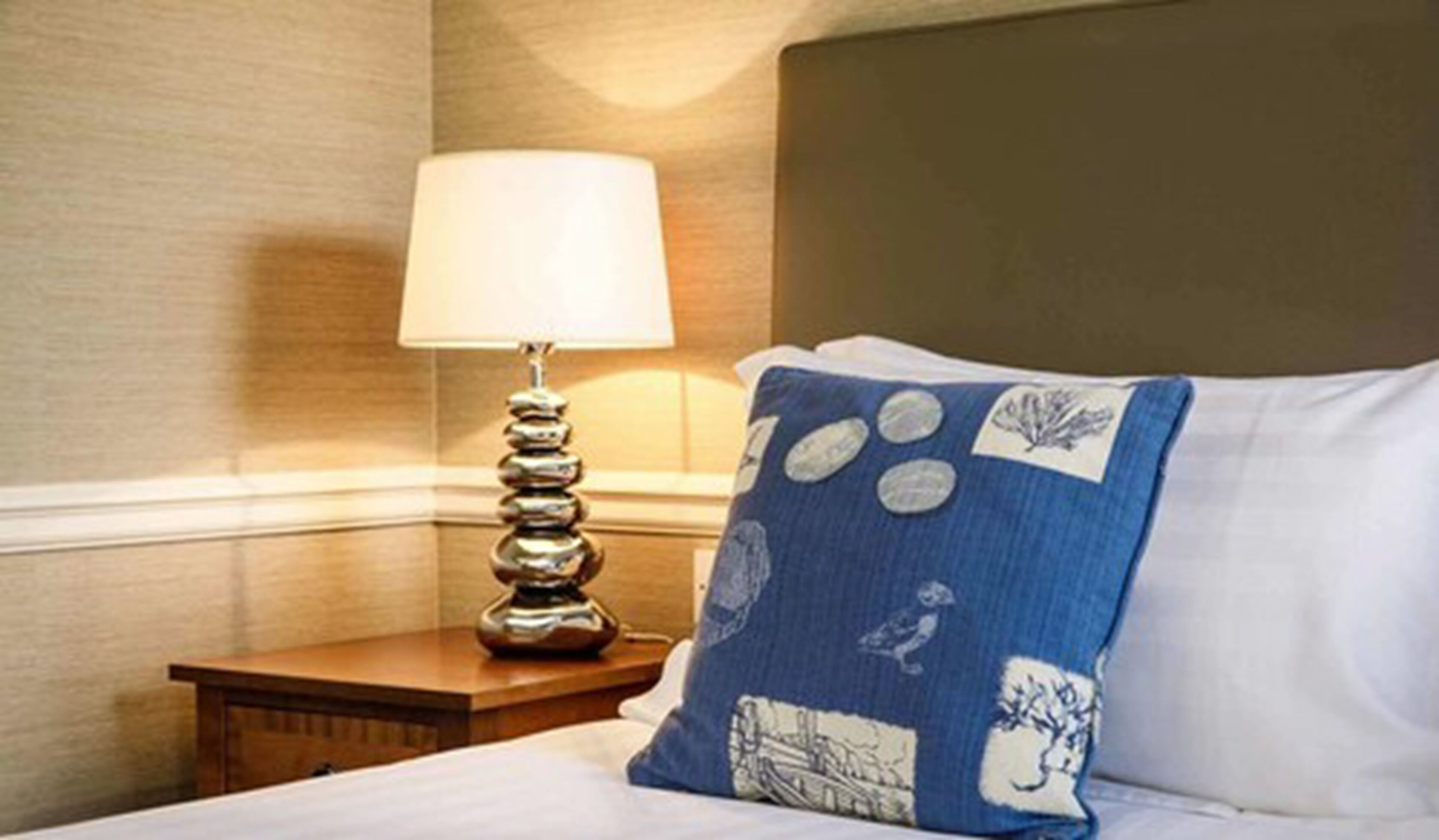 Una cama bien hecha con un almohadón blanco y uno azul con diseño náutico.