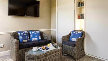 A cozy room with a sofa and armchair, a small round table with breakfast items, and a bookshelf with books.