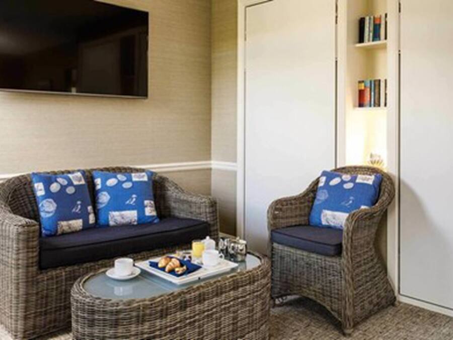 A cozy room with a sofa and armchair, a small round table with breakfast items, and a bookshelf with books.