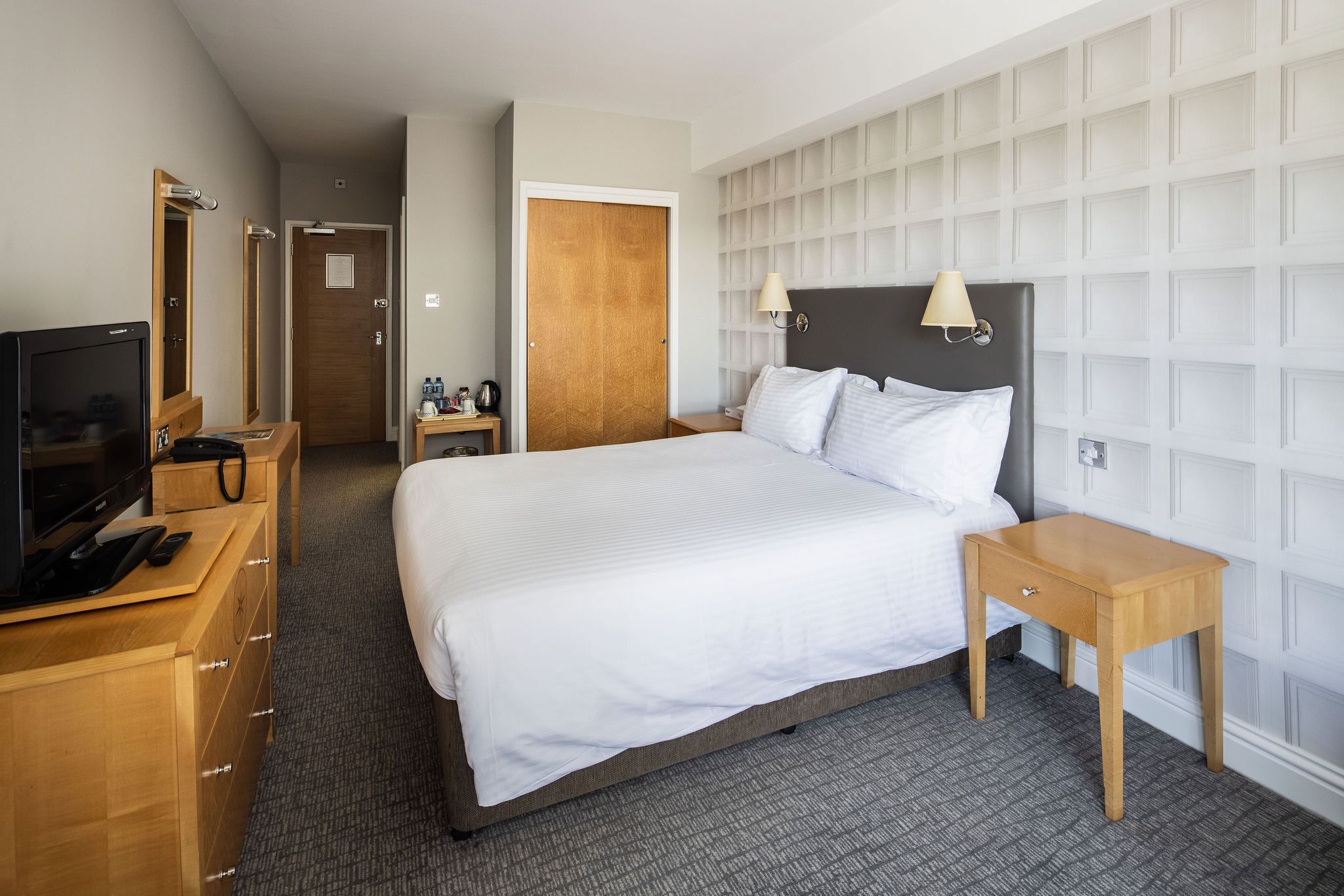 A hotel room with a large bed, a TV, a wooden dresser, and a nightstand.