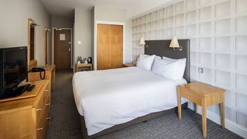 A hotel room with a large bed, a TV, a wooden dresser, and a nightstand.