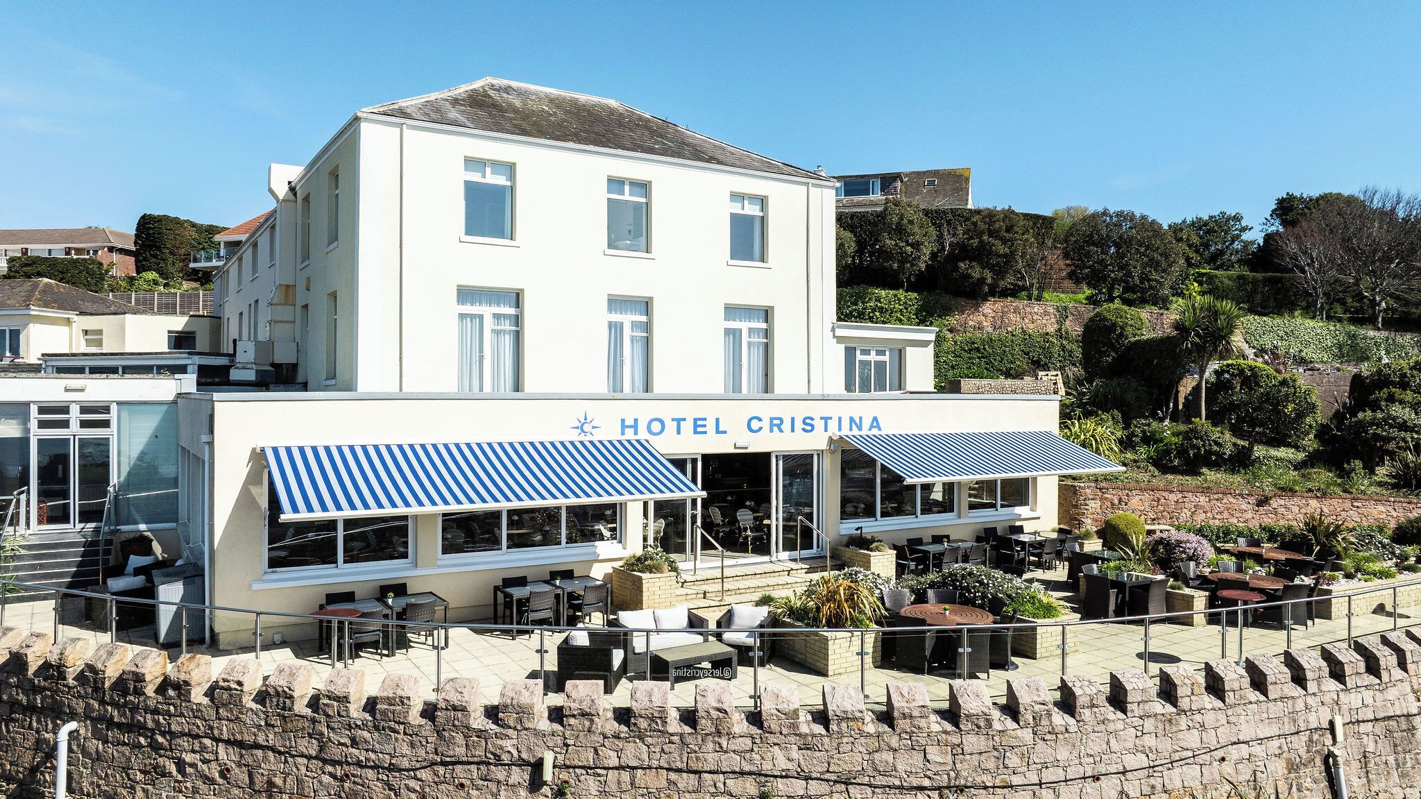 A hotel named 'HOTEL CRISTINA' with outdoor seating and a stone wall in the foreground.