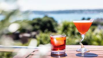 A martini glass and a highball glass on a wooden table with a blurred outdoor background.