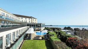 Et hotel med pool, udendørs siddepladser og havudsigt.