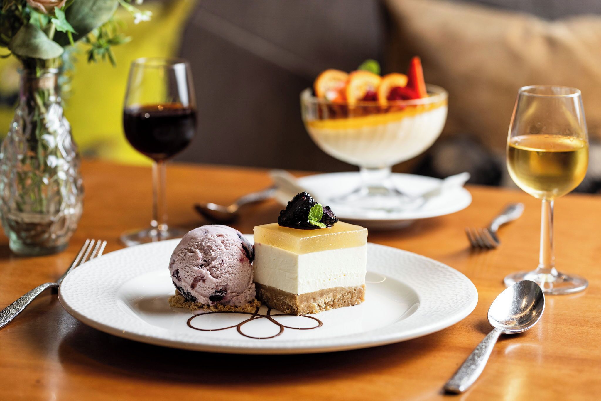 A dessert plate with ice cream and a layered cake, accompanied by wine glasses and cutlery on a wooden table.