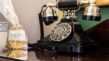 Un teléfono antiguo con dial giratorio, una taza de cerámica blanca con un diseño azul, y una bolsa de plástico que contiene una barra de pan con una etiqueta de advertencia de alérgenos.