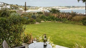 A patio with a table and chairs, a bottle of wine, and a view of the beach and ocean. - Somerville Hotel (St. Brelade)