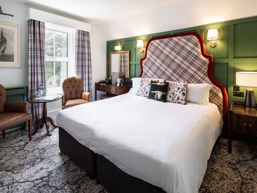Una habitación de hotel con una cama grande, un escritorio, una silla y una ventana con cortinas.