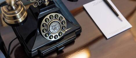 A vintage rotary dial telephone on a wooden table with a pen and a piece of paper nearby.