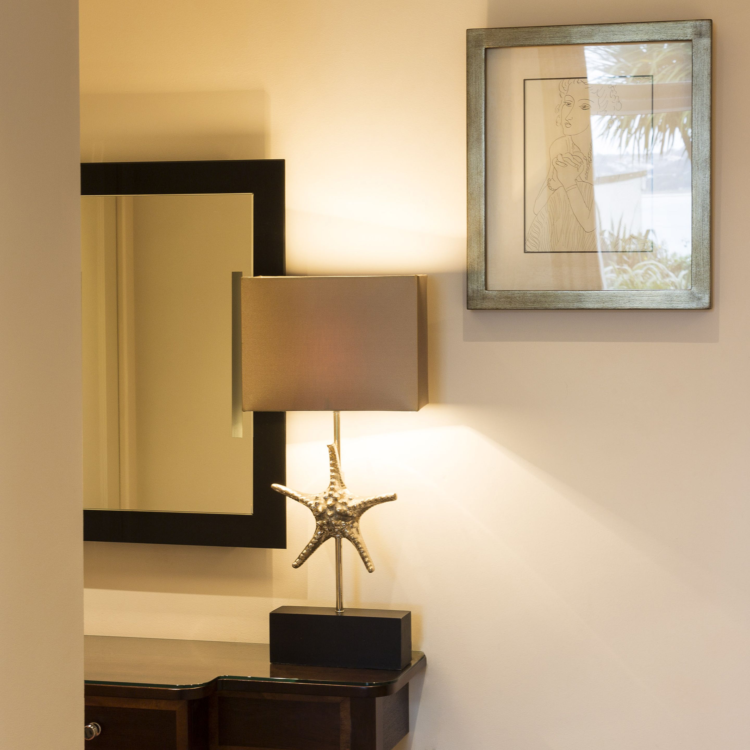 A room with a starfish lamp on a black stand, a framed picture on the wall, and a mirror with a black frame.