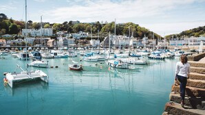 A marina with numerous boats docked, a person standing on the steps, and buildings in the background. - Somerville Hotel (St. Brelade)
