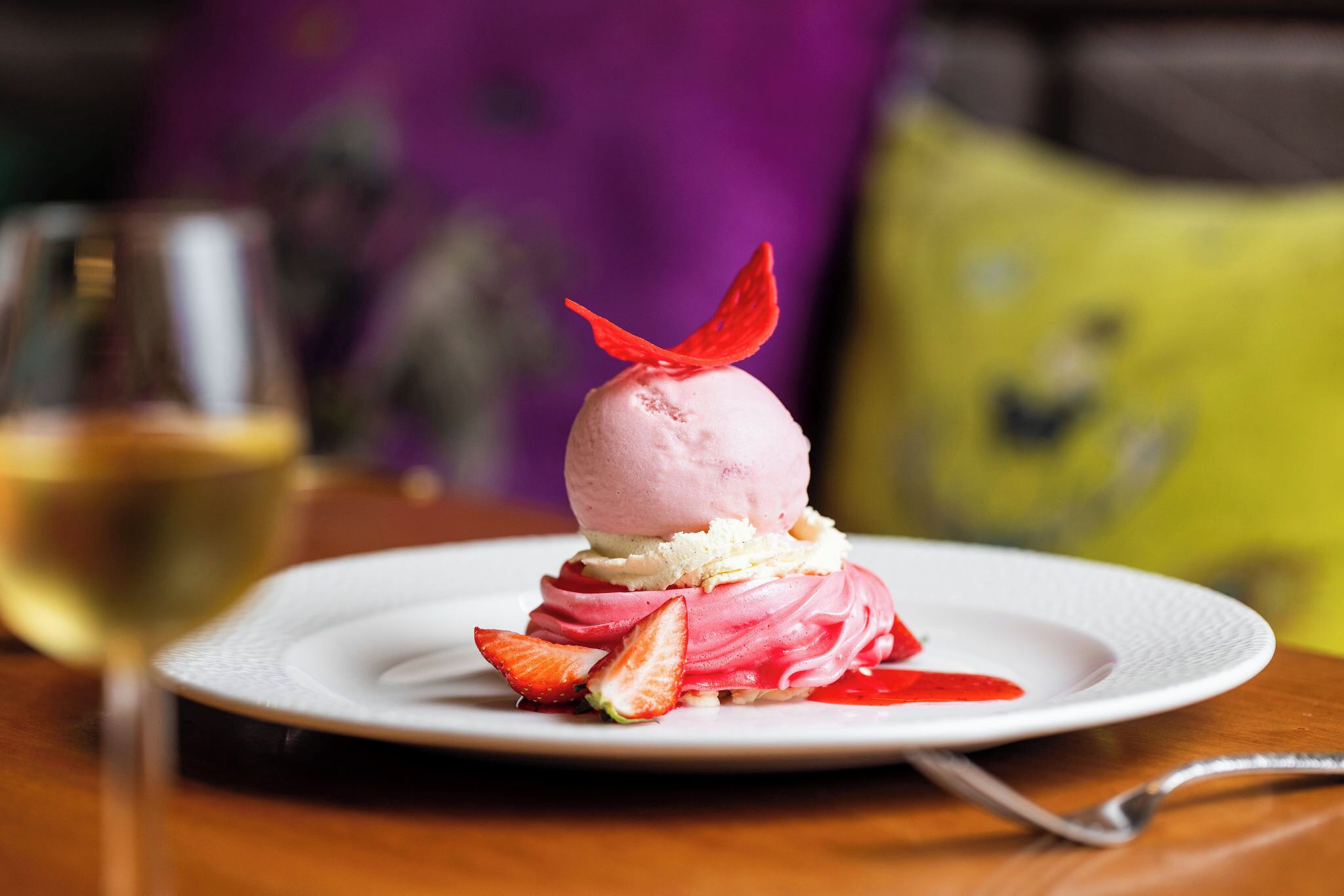 A dessert on a white plate with strawberries and a red leaf garnish.