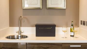 A kitchen with a stainless steel sink, a black Service en Chambre box, two framed artworks, and a bottle of Chablis wine.