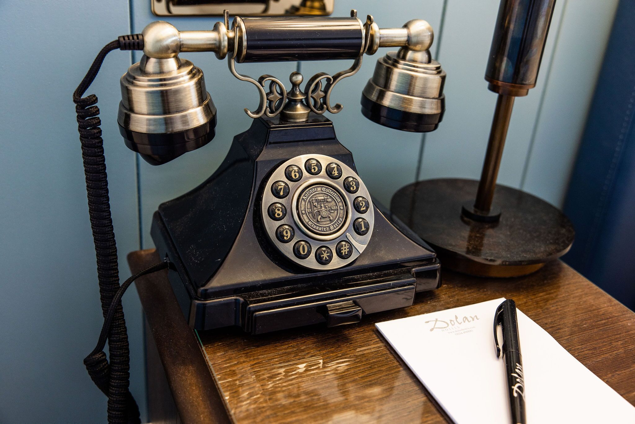 Een oude telefoon met draaiknop op een houten bureau, met een pen en een stuk papier waarop 'Botan' staat.