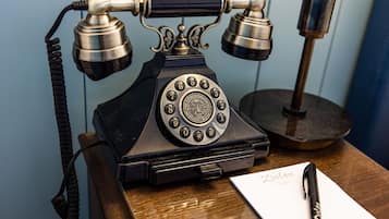 A vintage rotary dial telephone on a wooden desk with a pen and a piece of paper labeled "Botan."
