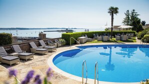 A pool with lounge chairs and umbrellas, surrounded by greenery and a view of the sea. - Somerville Hotel (St. Brelade)