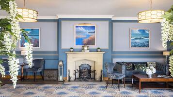A room with a fireplace, two armchairs, a sofa, a coffee table, and three paintings on the wall.