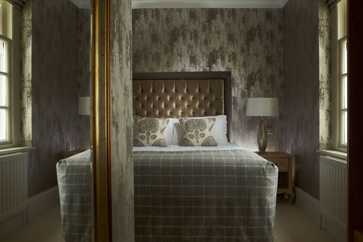A bedroom with a tufted headboard, a plaid bedspread, two bedside lamps, and a nightstand.
