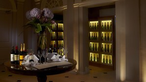 A luxurious interior with a round table set for dining, a vase of flowers, and a wine rack with bottles. - Brockencote Hall Hotel (Kidderminster)