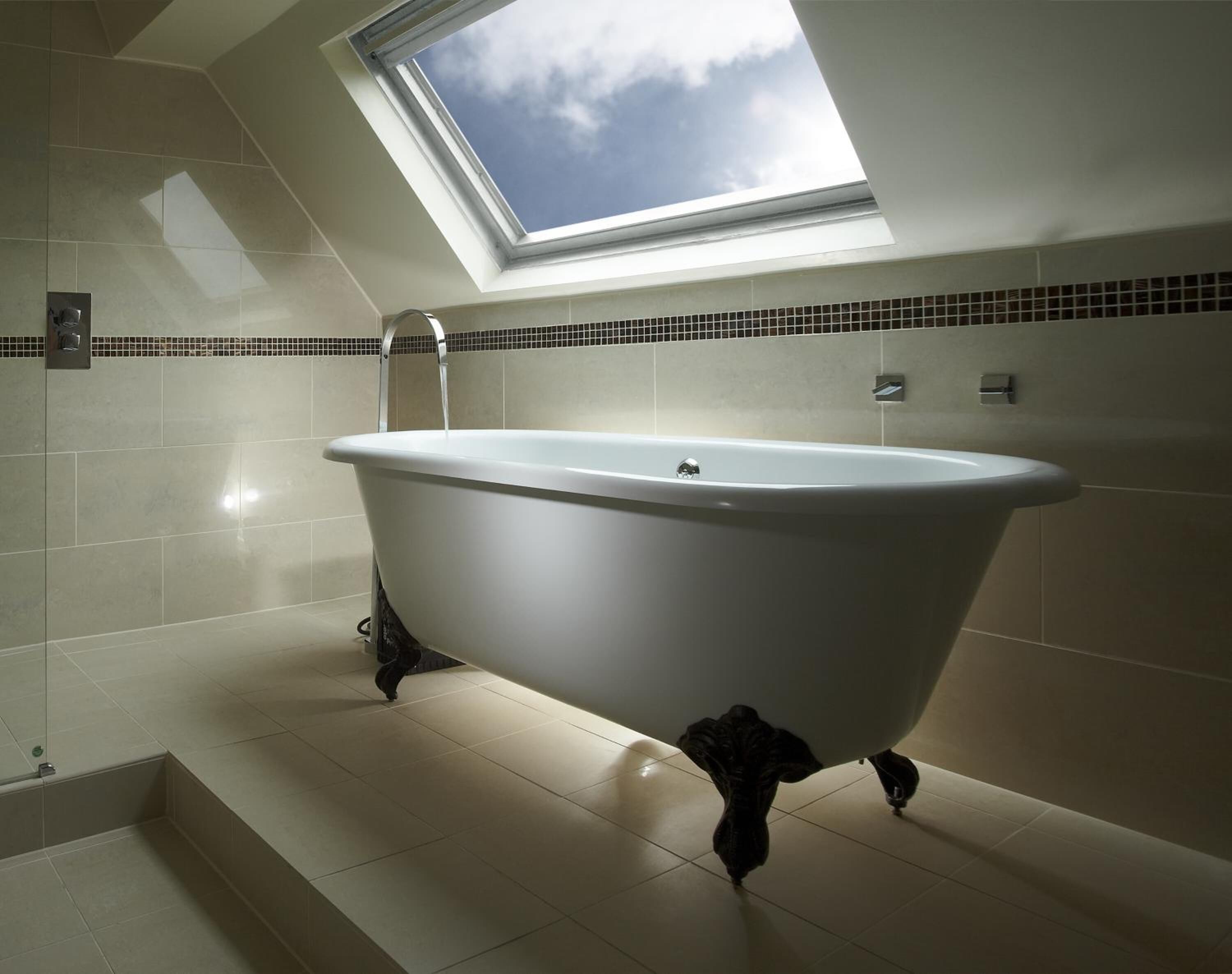 Une salle de bain moderne avec une baignoire sur pieds, un puits de lumière et des murs carrelés.