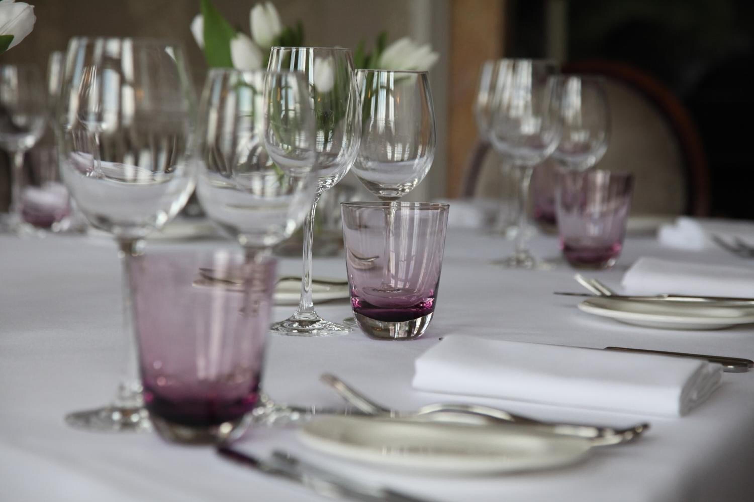 A table set for a formal dining occasion with multiple wine glasses and a purple glass centerpiece.
