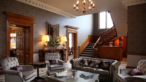 A spacious living room with a grand staircase, elegant furniture, and a chandelier. - Brockencote Hall Hotel (Kidderminster)