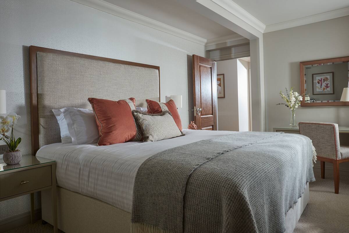 A neatly arranged bedroom with a large bed, a bedside table with a lamp, and a chair.