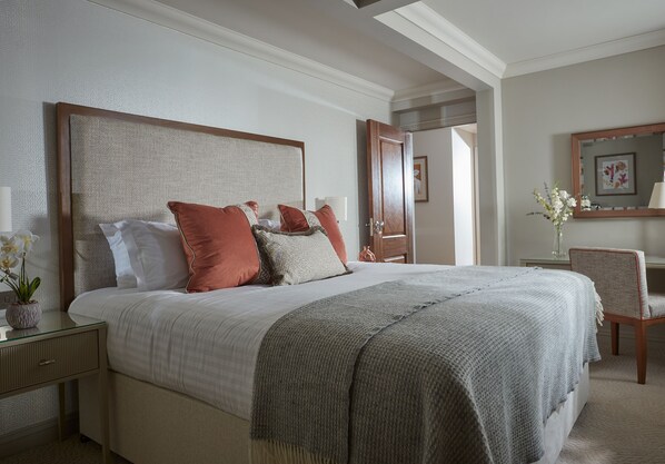 Un dormitorio ordenado con una cama grande, una mesita de noche con lámpara y una silla.