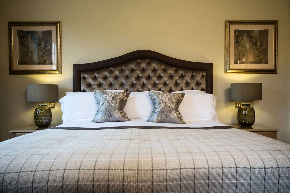 A neatly made bed with a tufted headboard, two bedside lamps, and two framed artworks on the walls.
