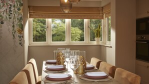 A dining room with a table set for six, a window with a view of greenery, and a kitchen area to the right. - Brockencote Hall Hotel (Kidderminster)