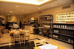 A restaurant with wooden tables and chairs, a counter with food items, and shelves with bottles and cups.