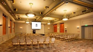 A conference room with rows of chairs, a projector screen, and a carpeted floor. - Austral Hotel (Comodoro Rivadavia)