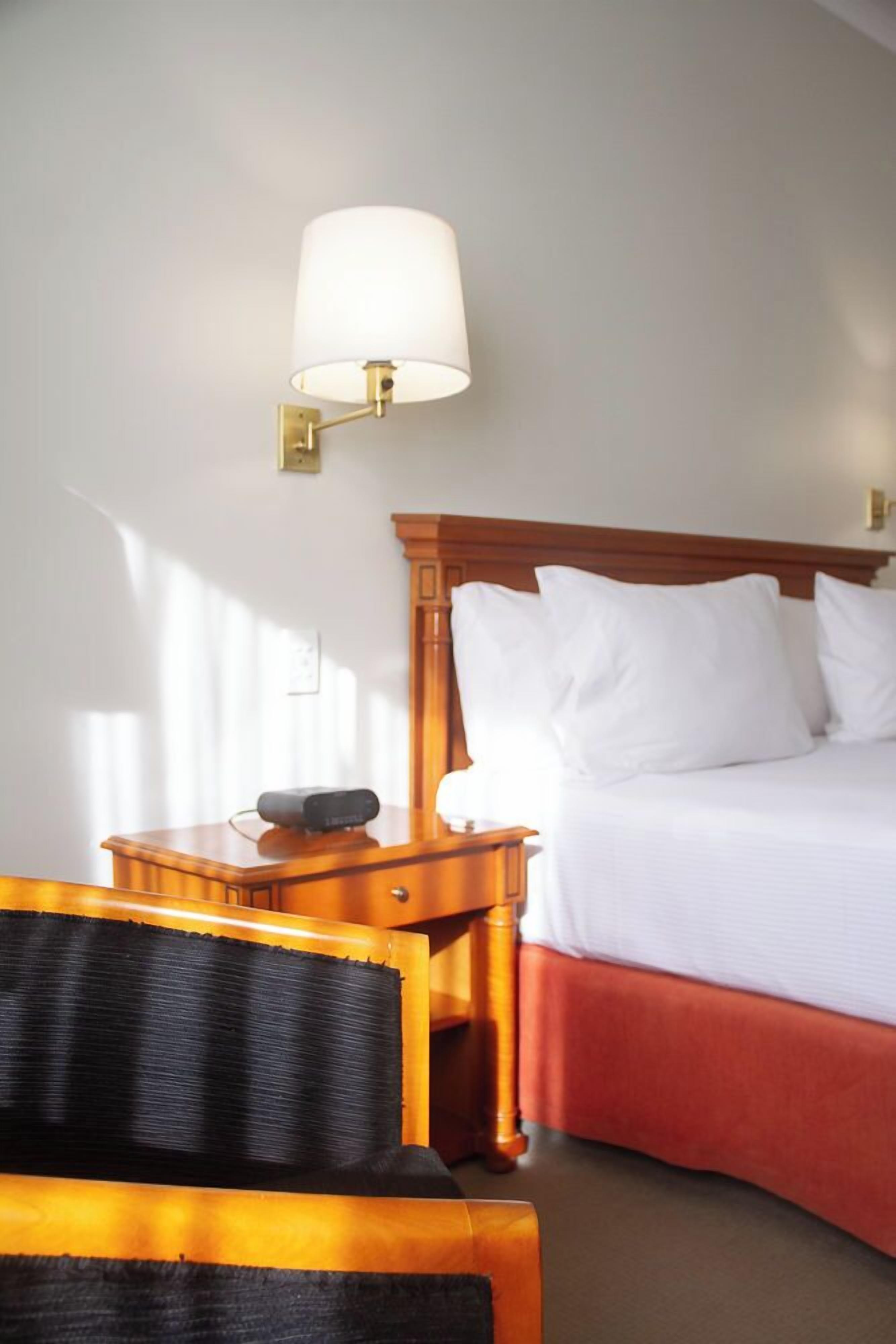 A hotel room with a wooden headboard, a bedside table with a lamp, and a bed with white linens.