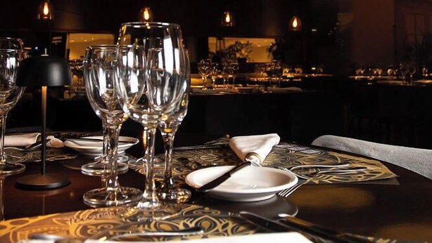 A dimly lit restaurant with a table set for two, featuring a patterned tablecloth and candlelight. - Austral Hotel (Comodoro Rivadavia)