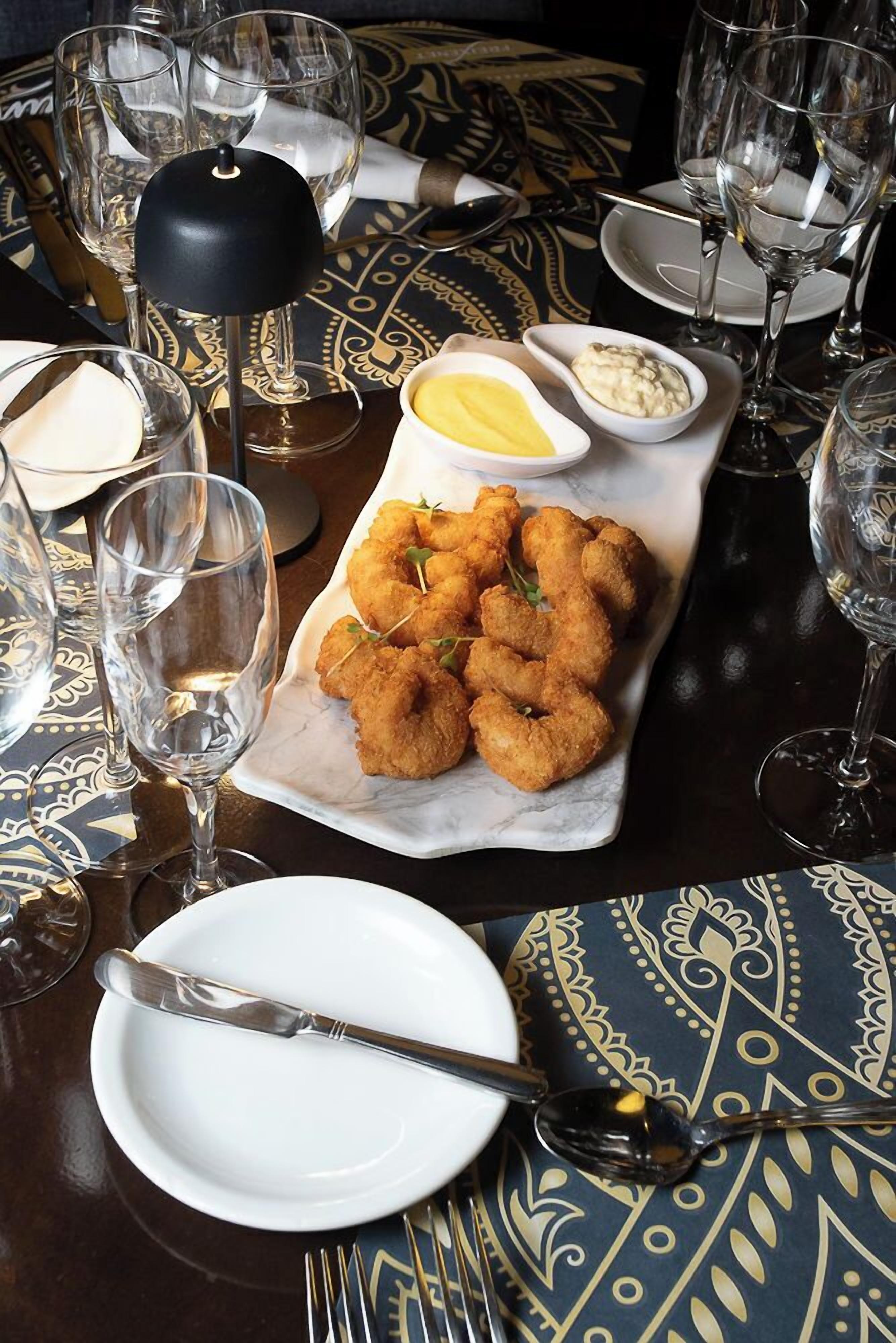 A dining table with a plate of fried food, a bottle of wine, and empty glasses.