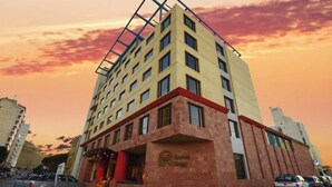 A multi-story hotel with a distinctive corner design, a visible entrance, and a parking area with vehicles. - Austral Hotel (Comodoro Rivadavia)