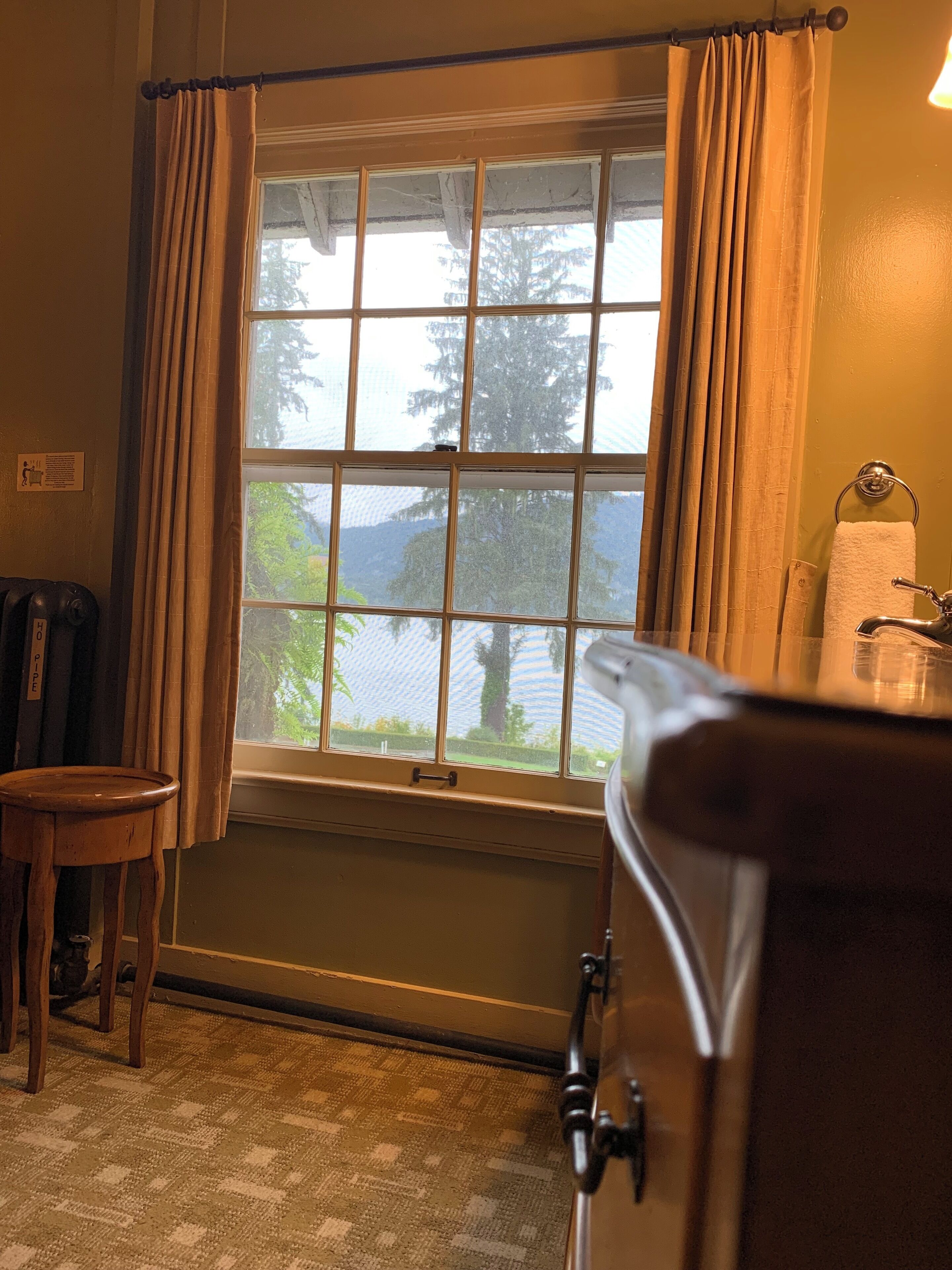 A room with a large window, a wooden stool, a radiator, and a towel rack.