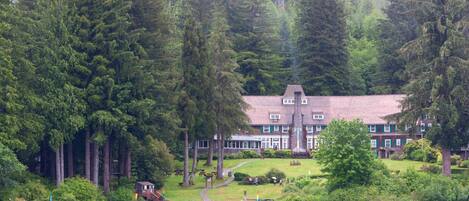 A lakeside lodge with a large building surrounded by dense forest, a dock with boats, and a clear view of the water.