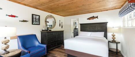 Un dormitorio con techo de madera, una cama con cabecera oscura, un sillón azul, un aparador y un espejo.