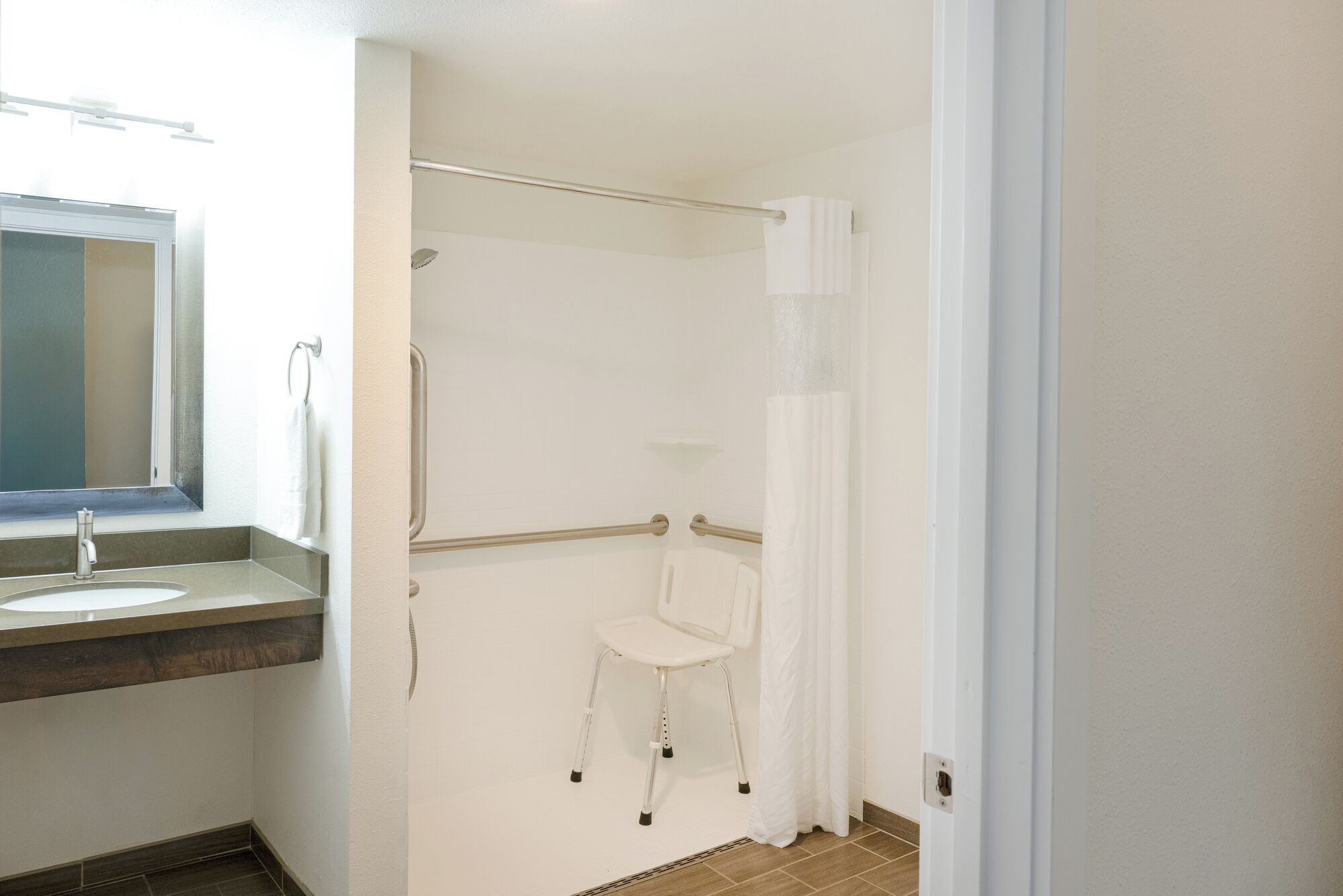A bathroom with a sink, mirror, shower, and a wheelchair-accessible chair.