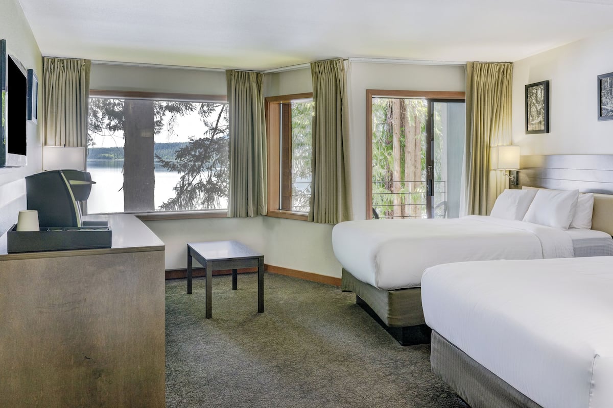 Une chambre d’hôtel avec deux lits, un bureau et une chaise. Elle est dotée de grandes fenêtres avec des rideaux, d’un téléviseur à écran plat et d’un tableau encadré au mur.