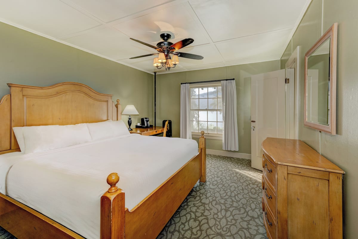 Une chambre d’hôtel avec un lit en bois, un ventilateur de plafond, une commode et une fenêtre avec des rideaux.
