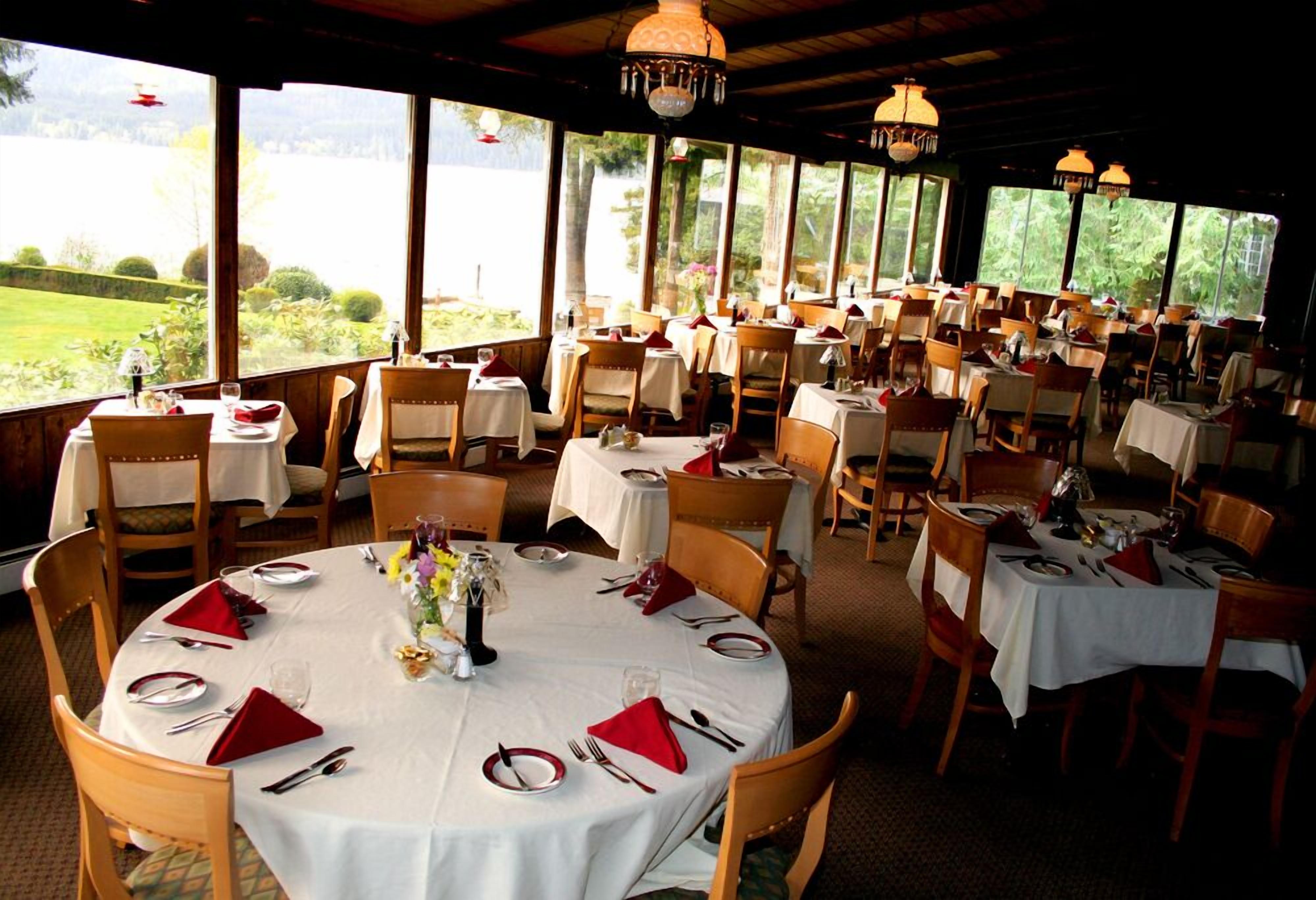 A restaurant with round tables set for dining, large windows offering a view of a green landscape, and hanging pendant lights.