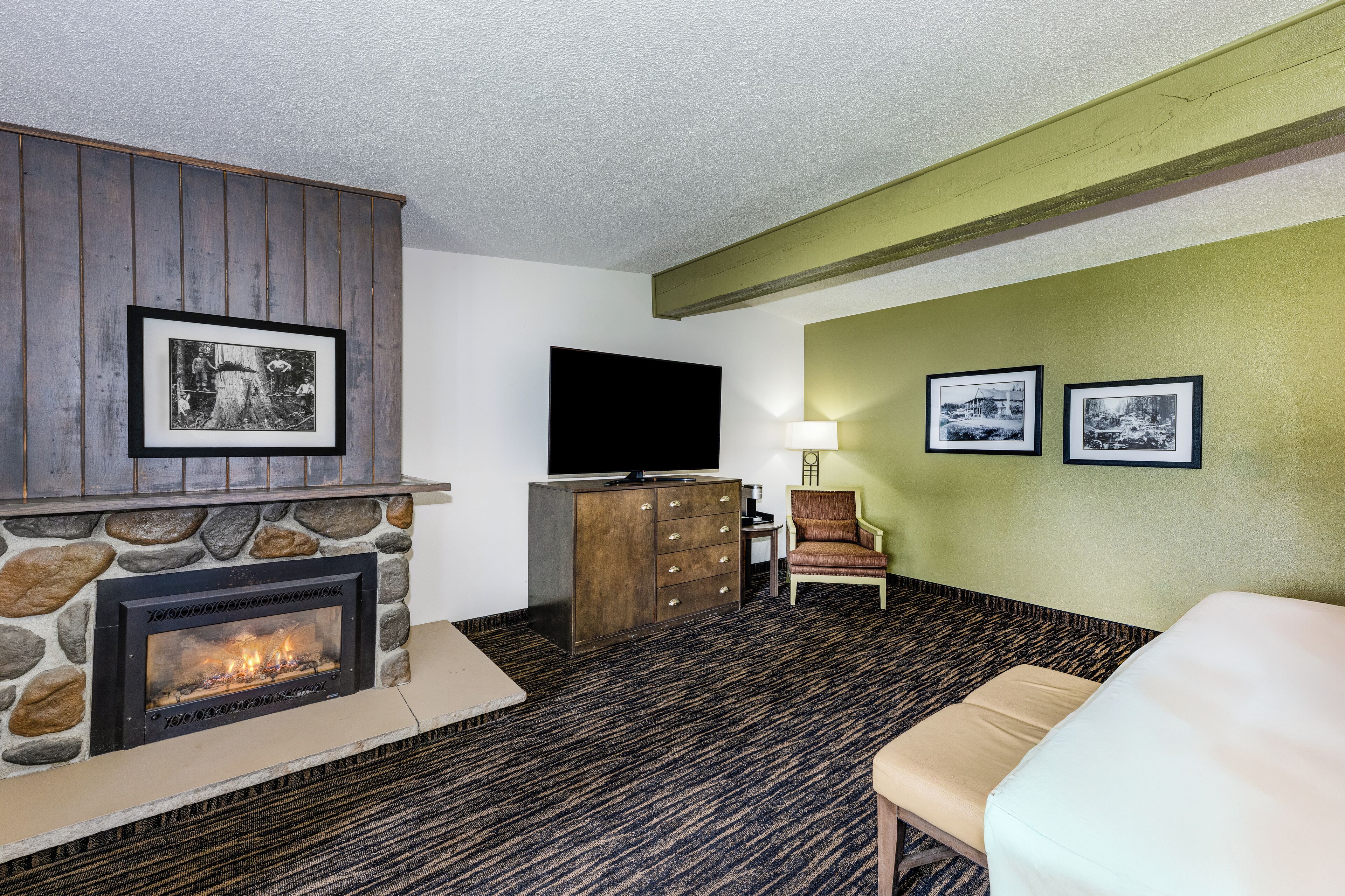 A living room with a stone fireplace, a television, a chair, and framed pictures on the wall.