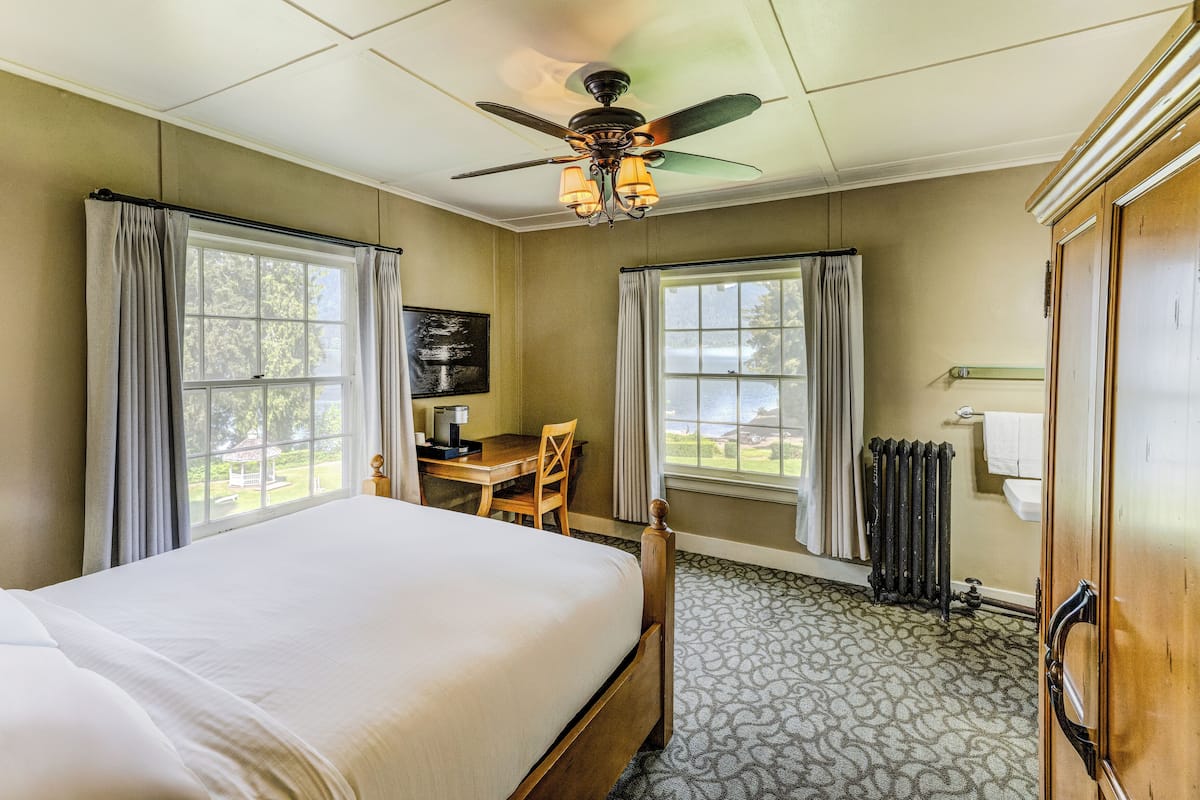 Une chambre d’hôtel comprenant un lit, un bureau, une chaise, un radiateur et une fenêtre donnant sur un belvédère.